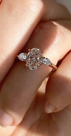 a woman's hand holding an engagement ring with three diamonds on top of it