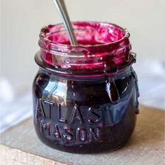 a glass jar filled with liquid sitting on top of a wooden table next to a spoon