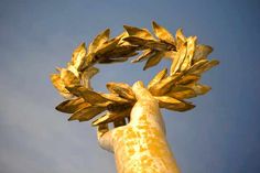 a golden statue with a wreath on it's head in front of a blue sky