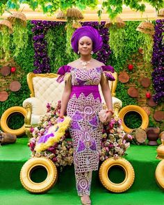 an african woman in a purple dress standing next to a couch and chair with flowers on it