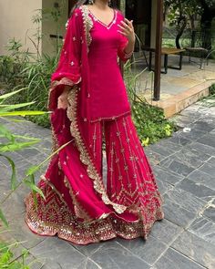 a woman in a pink outfit standing on a stone walkway with her hand up to her face