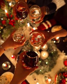 several people toasting with glasses of wine in front of a christmas tree and ornaments