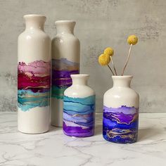 three vases with flowers in them sitting on a marble counter top next to each other