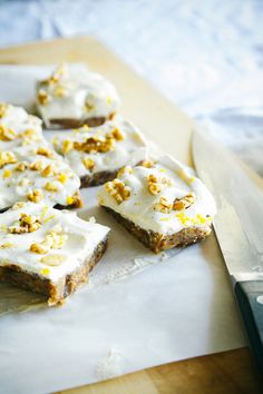 several pieces of cake with white frosting and walnuts on top next to a knife