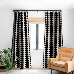 a chair sitting in front of a window with black and white curtains