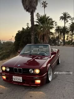 a red convertible car parked on the side of a road next to trees and palm trees