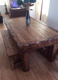 a wooden table sitting on top of a hard wood floor next to a vase filled with flowers