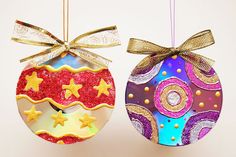 two christmas ornaments hanging from strings on a white background with gold and red decorations in the shape of stars