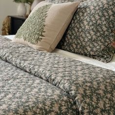 a bed with two pillows on top of it next to a night stand and lamp