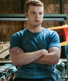 a young man sitting in front of a desk with his arms crossed and looking at the camera