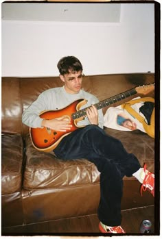 a man sitting on top of a brown couch holding an electric guitar next to him