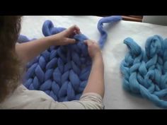 a woman is weaving blue yarn on a table with two large pieces of fabric in the background