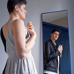 a woman standing in front of a mirror looking at her reflection wearing a leather jacket