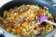 a pot filled with meat and vegetables on top of a stove next to a purple spatula