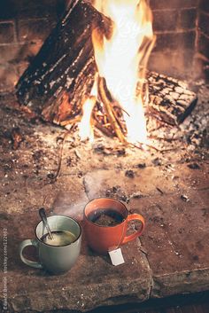 two cups of coffee sitting in front of a fire