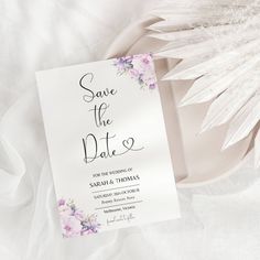 a wedding save the date card on a plate with white feathers and pink flowers in it