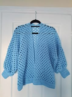 a blue crocheted sweater hanging on a white door with a black hanger