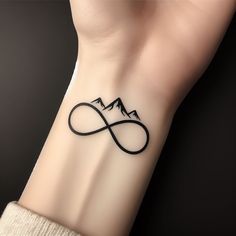 a tattoo on the wrist of a woman with mountains in the background and an infinite symbol