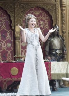 a woman in white dress standing on stage with her arms out and one hand outstretched