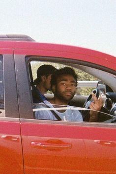 two men sitting in the drivers seat of a red car