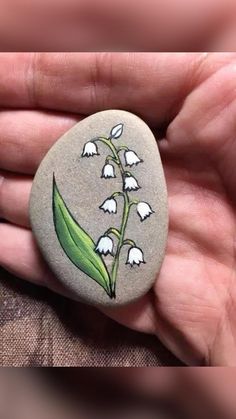 a hand holding a rock with flowers painted on it and an arrow in the middle