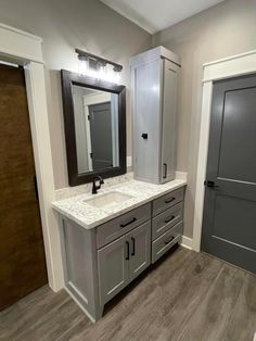 a bathroom with gray cabinets and white marble counter tops, along with a large mirror on the wall