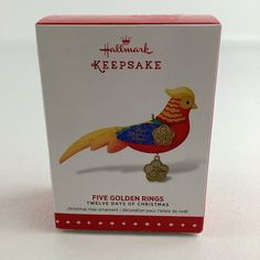 a red and yellow bird ornament on a white box with the words, five golden rings