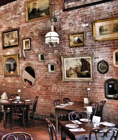 an empty restaurant with tables and chairs in front of a brick wall that has pictures on it