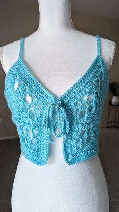 The "Azure Blossom Top" is a charming handmade crochet piece that combines elegance with a playful vibe. Crafted in a vibrant blue yarn, this top features an intricate floral motif that adds a touch of sophistication to its design. The delicate ties at the front provide both style and adjustability, ensuring a perfect fit. Ideal for pairing with high-waisted shorts or a flowing skirt, the Azure Blossom Top is a versatile addition to any summer wardrobe, perfect for beach outings, music festivals, or casual daytime wear. CUSTOM MADE ORDER: Choose the color, size, and material for a unique product. Experience the perfect combination of style and functionality with custom options tailored to your liking. Color: Aqua Green Material: Acrylic  Size: Small Measurements in inches: 18" across chest Blue Bohemian Top With Crochet Trim, Summer Crochet Lace Top Made Of Yarn, Blue Crochet Lace Top, Blue Lace Crochet Top, Blue Lace Crochet Top For Summer, Blue Bohemian Lace Top, Blue Lace Sleeveless Tops, Sleeveless Blue Lace Tops, Blue Lace Tops For The Beach