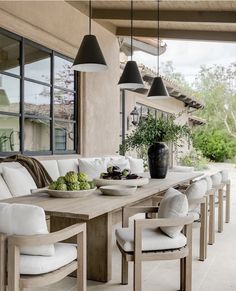 an outdoor dining area with white cushions and wooden table surrounded by chairs, potted plants and hanging lights