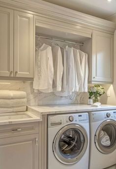 a washer and dryer in a white laundry room with lots of hanging clothes