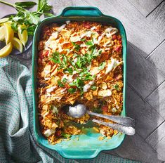 a casserole dish with meat and vegetables in it on a blue towel next to lemon wedges