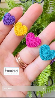 a person is holding three crocheted hearts on their fingers and two rings are in the foreground