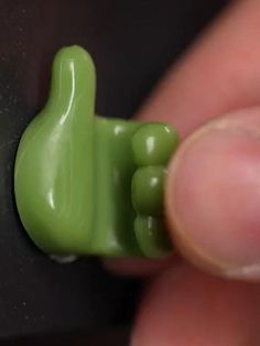 a small green toy like object being held by someone's thumb with their thumb