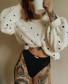 a woman with tattoos is drinking from a coffee cup while wearing high waisted shorts