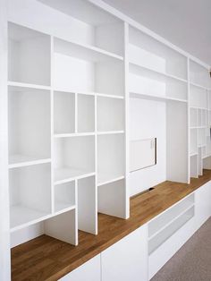 a white bookcase with wooden shelves in an empty room next to a carpeted floor