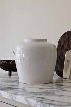 a white vase sitting on top of a counter next to a cutting board and bowl