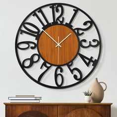 a clock that is on the wall next to a table with a vase and books