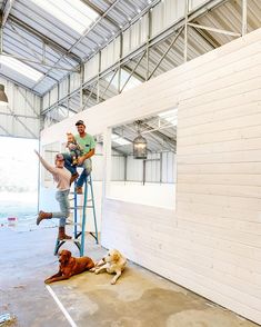 two men and a dog are sitting on a ladder in an industrial building while another man is standing next to them