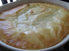 a close up of a pie in a white dish on a table with a window behind it