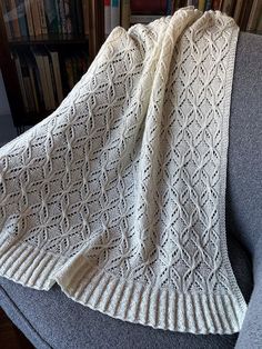 a white knitted blanket sitting on top of a gray couch next to bookshelves