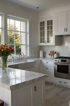 a white kitchen with marble counter tops and stainless steel appliances, along with an island in the middle