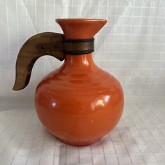 an orange vase sitting on top of a white tile floor next to a wooden handle