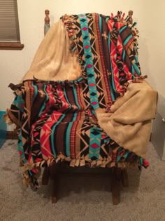 a chair covered with a colorful blanket on top of it's back legs in front of a white wall