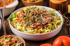 a white bowl filled with pasta and meat on top of a table next to bowls of vegetables