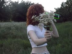 a woman standing in a field holding flowers and a beer bottle with her mouth open