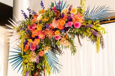 an arrangement of flowers and greenery is displayed on a tall pole in front of a white curtain