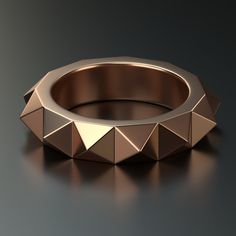 a gold ring with pyramids on the inside and outside, sitting on a black surface