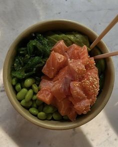 a bowl filled with meat and vegetables on top of a white counter next to chopsticks