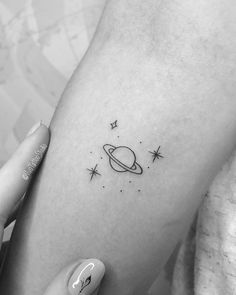 a small saturn tattoo on the left inner arm, with stars in the sky above it